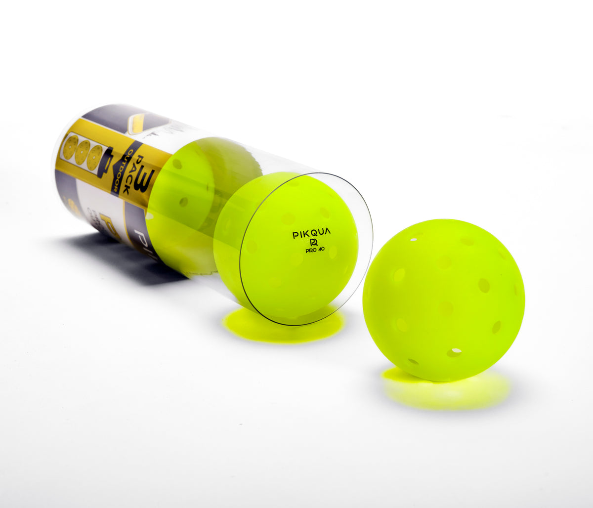 A bright neon yellow-green pickleball shown outside its clear plastic tube packaging, with another two balls visible inside and a branded labeled Pikqua Pro 40 on the tube, photographed on a clean white background.