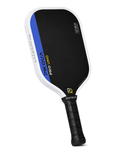 A pickleball paddle with a black paddle face, white border with NYC skyline, blue accent stripe, and black grip handle. The paddle features the brand name 'PIKQUA' and model 'PRO UNO KEVLAR' on the face, along with IPMA certification logos.